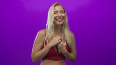 Kırmızı dantelli üstteki kadın iki eliyle yüzük kutusunu açıyor ve stüdyoda canlı mor arka planda gülümsüyor..