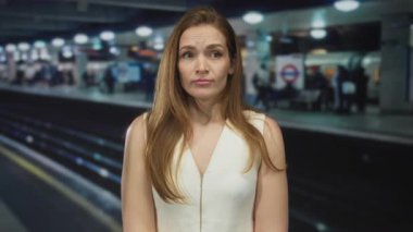 İstasyondaki tren raylarının yanında çıplak kollarıyla ayakta duran kadın tarafsız bir ifadeyle, sabırsız..