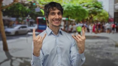 Genç adam gündüz saatlerinde taştan boynuzlar yapıyor ve kalabalık şehir caddesinde gülümsüyor..