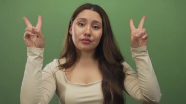 Genç İspanyol kadın dudaklarını büker, kaşlarını kaldırır ve yeşil stüdyoda tırnak işareti için parmaklarını çimdikler..
