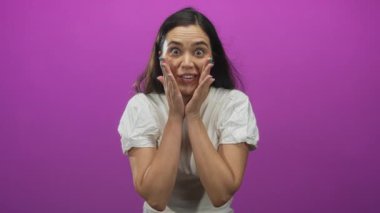 Mor bir stüdyoda beyaz gömlek giyen bir kadın geniş gözlü ve açık ağızlı yanakları tutuyor. Sürpriz..
