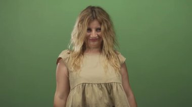 Kadın başını arkaya eğip çıplak boynunu gösteriyor ve yeşil stüdyoda parlak bir gülümseme ile bronz bir elbise giyiyor..