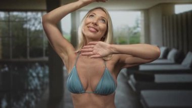 Kadın kollarını başının üstüne kaldırıyor göğsünü gösteriyor ve spa havuzu binasında yumuşak ışık altında gülümsüyor; huzur mutluluğu..