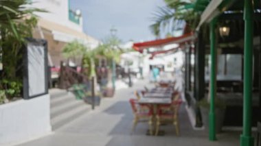 Ianzarote 'de odanmamış bir açık hava sahnesi, güneşli havada masalar, sandalyeler, palmiye ağaçları ve şemsiyelerle kaplı büyüleyici bir caddenin bulanık bir görüntüsü..