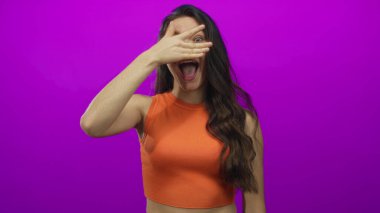 Portakallı bluzlu genç İspanyol kadın mor bir stüdyoda gözlerini kapatıyor..