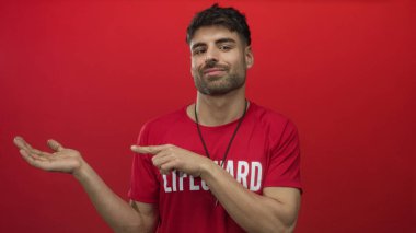 Kırmızı cankurtaran tişörtü giyen İspanyol genç cankurtaran kırmızı stüdyoda çıplak elle işaret ediyor..