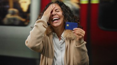 Tren istasyonunda elinde mavi kredi kartıyla gülümseyen bir kadın bulanık bir tren geçmişine karşı duygu ve modern şehir yaşam tarzını yakalıyor..