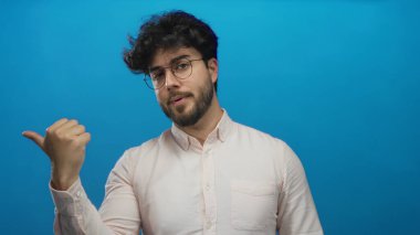 Sakallı ve gözlüklü genç İspanyol bir adam canlı mavi bir arkaplan önünde jestler yapıyor, bir dizi dinamik pozlarla yön, odak ve karar ifadelerini vurguluyor..