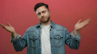 Kot gömlekli sakallı genç adam ellerini kırmızı arka plan duvarına dayayıp belirsizlik gösteriyor..