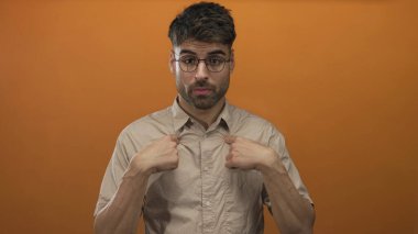 Stüdyoda parlak turuncu arka planı olan bir gömlek yakasını gösteren bir adam parmağı, meraklı bir bakışla çerçevelenen gözlükler; şüphe..