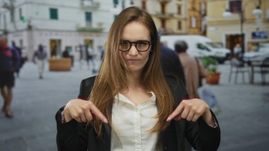 İşlek şehir caddesinde arka planda bulanık yayalar olan iki işaret parmağıyla kaldırımı gösteren bir kadın..