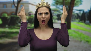 Güneşli bir park ortamında şen şakrak yüzler yapan İspanyol bir kadın. Etrafı gür ağaçlar ve canlı yeşilliklerle çevrili. Neşeli ve spontane bir hava yayıyor..