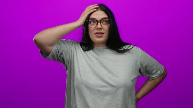 Gözlüklü genç ve cüsseli bir kadın canlı pembe bir arka plan duvarına karşı güvenle poz veriyor..