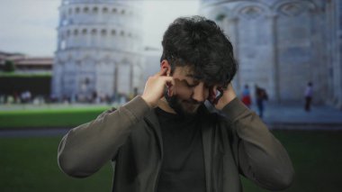 Sakallı genç adam güneşli bir günde sidik kulesinin önünde kulaklarını kapatıyor İtalya 'da bir ifade anı yakalıyor..