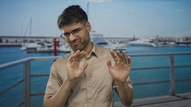 Adam, güneşli liman limanındaki liman iskelesinde beyaz teknenin tiksindirici ifadesiyle avuçlarını itiyor..