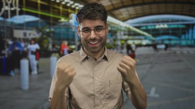 Günışığı havaalanı terminalinde gözlük takan genç İspanyol adam yumruk kaldırıyor; seyahat heyecanı.
