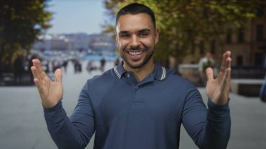 Arkasında bulanık binalar olan güneşli bir şehir caddesinde uzanmış elleri açık gülümseyen bir adam neşeyi paylaşıyor..