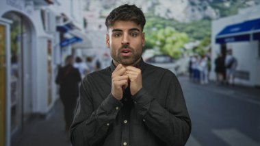 Koyu renk tişörtlü genç İspanyol adam, geride bulanık yayalar bırakarak çenesine yakın yumruklarını sıkıyor..