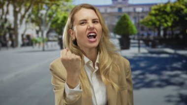 Güneşli bir şehir caddesinde, ağaçlar ve binalarla çevrili bulanık bir şehir arka planının önünde duygularını ifade eden bir kadın..