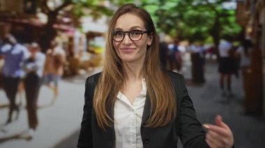 Siyah ceketli ve beyaz gömlekli genç kadın, bulanık kalabalığın ortasında şehir caddesinde başparmak kaldırıyor..