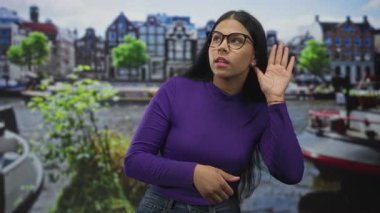 Mor kazaklı bir kadın, şehir caddesinde bir kanalın yanında el ele tutuşuyor. Merak uyandıran bir şey var..