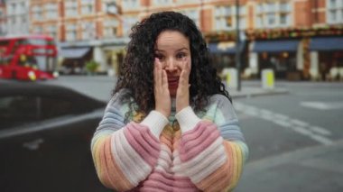 Arka planda ikonik kırmızı çift katlı otobüsle renkli bir caddede elleri yanaklarında neşe ifade eden kadın..