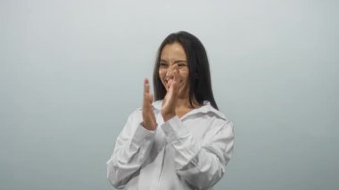 Genç bir kadın el çırpıyor ve açık gri bir stüdyoda gülümsüyor beyaz gömlek ve çiller giyiyor; sevinç kutlaması.