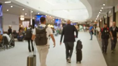 Dolu havaalanı terminalinde parlak ışıklar ve arka planda çeşitli dükkanlarla yürüyen bulanık insanlar