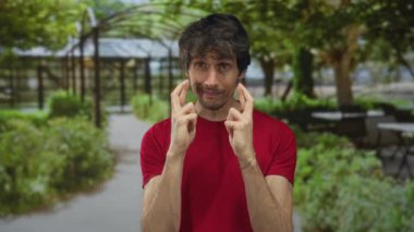 Kırmızı gömlekli adam, yaprakların arasından süzülen güneş ışığı gibi yeşil gölgelik altında parmaklarını çaprazlar ve orman patikasında gözlerini kapatır..