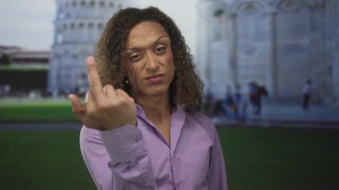 Kıvırcık saçlı transseksüel kadın açık havada sidik binasının eğimli kulesinde orta parmağını sallıyor..