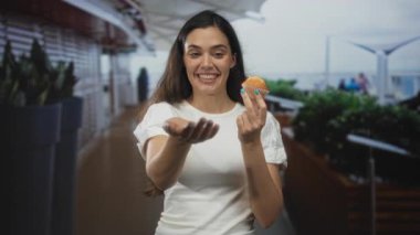 Beyaz bluzlu genç İspanyol kadın bina içinde kek tutarken gülümsüyor ve yardım eli uzatıyor..