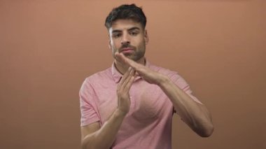Pembe polo tişört giyen genç İspanyol adam stüdyoda elleri ile zaman geçirme hareketi yapıyor; ciddi yansıma.