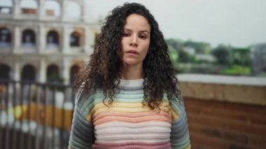 Renkli kazaklı, kıvırcık saçlı genç İspanyol kadın Roma, İtalya 'daki sembolik Roma kolezyumunun önünde kollarını kavuşturuyor..