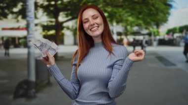 Elinde İsviçre banknotları olan bir kadın, arka planda ağaçlarla bir caddede gülümsüyor. Mutluluk ve kendine güven saçıyor. Günlük mavi bir süveter giyiyor..