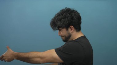 Sakallı genç bir adam mavi bir arka plana ip çekiyor gibi yapıyor, oyuncu ve yaratıcı bir aksiyon konseptini tasvir ediyor..