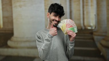 Norveçli Krone 'u elinde tutan adam eski bir üniversitede açık havada para yatırıyor, akademik bir ortamda kendine güvenen bir ifadeyle para gösteriyor..