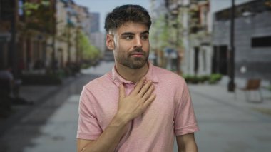 Erkek debriyaj göğüs jesti samimi bakışlar ve samimi pembe polo gömlek ile şehir sokak; minnettarlık.