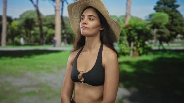 Hasır şapkalı kadın, ormandaki açık yeşil ağaçların arasında dururken saçına dokunuyor. Huzur..