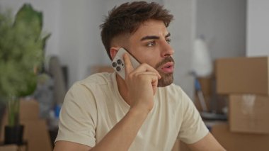 Adam binanın içindeki kutuları açarken masaya yaslanırken akıllı telefonu kulağına tutuyor; tefekkür.