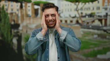 Stresli, sakallı, Roma harabelerinde dikilen kot giyen, etrafındaki tarihi atmosferden bunalmış genç bir adam..