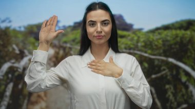 Parktaki İspanyol kadın, arka planda yeşillik ve açık hava ortamındaki vaat ve bağlılığı simgeleyen bir taahhüt jesti yapıyor..