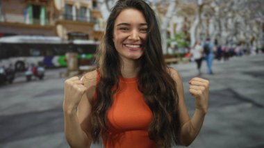 Turuncu bluzlu genç İspanyol kadın otobüsün yanındaki işlek güneş ışığı altındaki sokak köşesinde pazılarını esnetiyor..