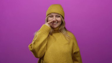 Hardal süveter giyen ve bereli bir kadın burnuna dokunuyor canlı pembe bir fon, neşeli bir cazibe ve sıcaklıkla basit bir stüdyo ortamında yayılıyor..