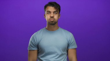 Genç adam yanaklarını şişiriyor ve parmaklarını izole edilmiş mor arkaplan önünde dokunduruyor..