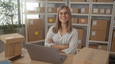 Binanın içinde depolama rafları ve bant ile çevrili paketler ve paket kutularıyla yazan kadın; başlangıç hırsı.