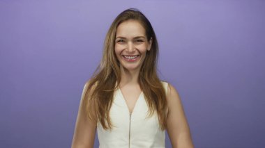 Görünür dişleriyle gülümseyen ve mor stüdyo ortamında çıplak omuzlarıyla başını eğen bir kadın. Mutluluk..