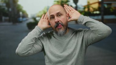 Kel adam şehir sokaklarında poz verirken komik suratlar yapıyor. Gri bir gömlek ve sakal takıyor. Şehir ortamında gün ışığında yakalandı..