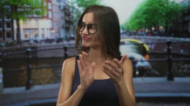 Kanal kenarında Amsterdam caddesinde çıplak kollarıyla gülümseyen ve el çırpan bir kadın..