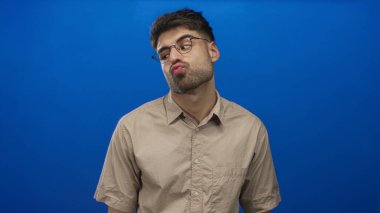 Erkekler dudaklarını büzer ve mavi duvara karşı stüdyoda yuvarlak gözlük takarak kaşlarını kaldırır..
