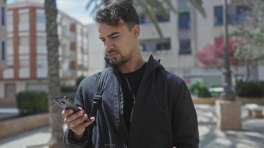 Etrafı yeşillik ve binalarla çevrili güneşli bir parkta akıllı telefonlara bakan genç İspanyol bir adam, gelişigüzel ve kentsel bir yaşam tarzını aktarıyor..